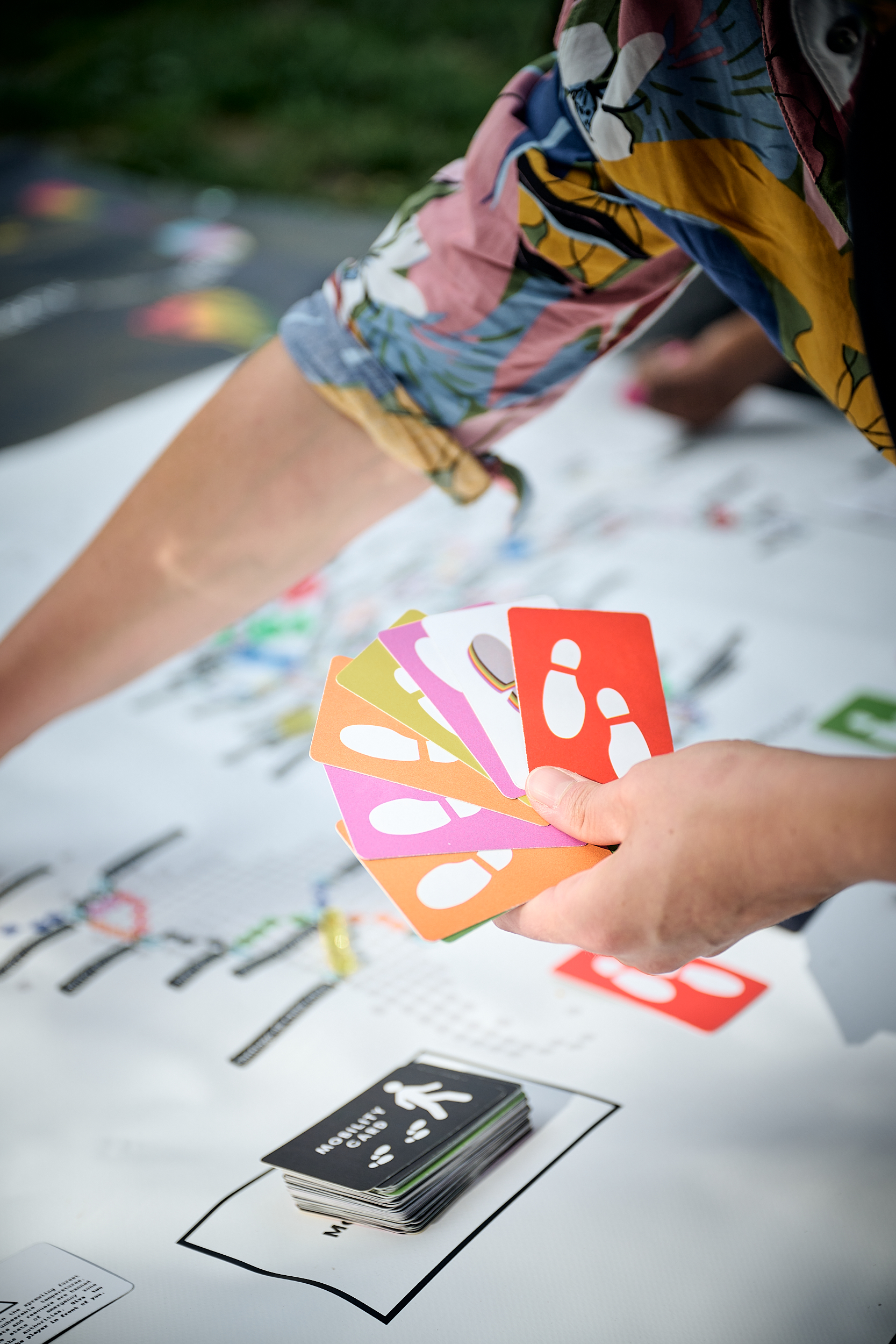A player holding a fan of colourful Mobility Cards above the One Way Ticket board